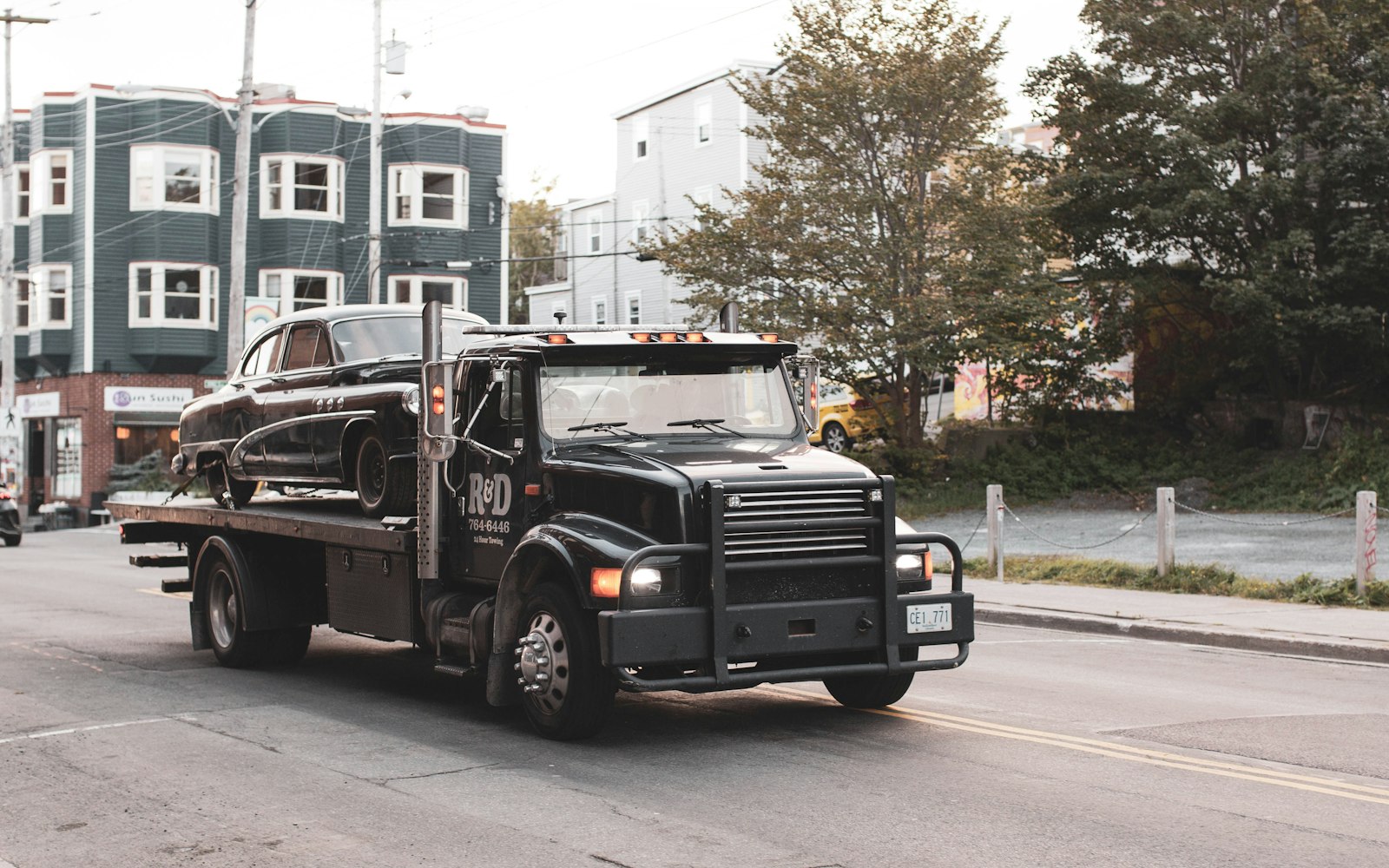 A flatbed hauler carrying a single classic car through a city street